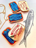 five Sardine necklaces grouped together around the original ink hand drawing of a sardine, that the necklace was designed from