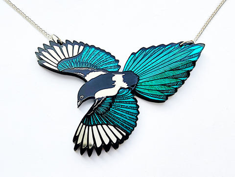 A silver chain necklace featuring a detailed magpie pendant with spread wings in vibrant teal, black, and silver mirror on a clean white background.